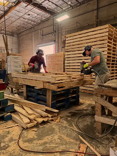 Two workers assembling a wooden pallet inside the production facility